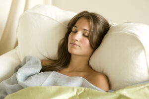 - Marion Salon Spa in Salt Point, NY A woman rests peacefully with her eyes closed against soft white pillows in a serene, softly lit setting. - Marion Salon Spa in Salt Point, NY