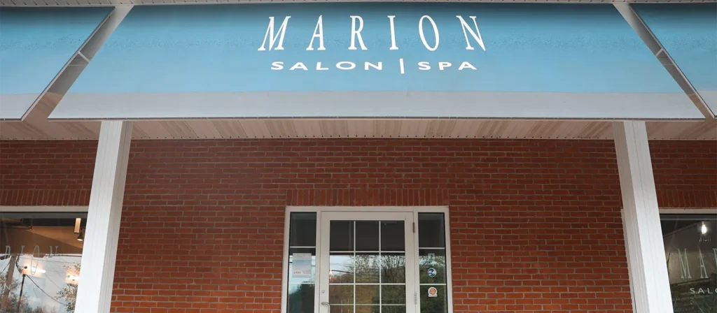 - Marion Salon Spa in Salt Point, NY Front entrance of Marion Salon Spa with glass double doors, brick walls, and a blue awning displaying the name "Marion Salon Spa" in white uppercase letters—your destination for deluxe hydrafacial skin treatment and deep tissue massage therapy. - Marion Salon Spa in Salt Point, NY