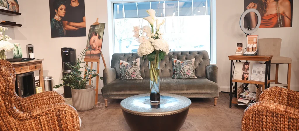 - Marion Salon Spa in Salt Point, NY A cozy salon waiting area with a velvet sofa, wicker chairs, a round table with flowers, and beauty product displays near a large window sets the perfect ambiance for clients awaiting their hand-tied hair extensions or deluxe hydrafacial skin treatment. - Marion Salon Spa in Salt Point, NY