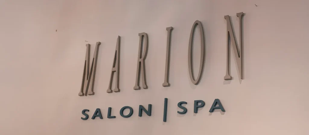- Marion Salon Spa in Salt Point, NY Wall sign displaying "MARION SALON SPA" in large, raised letters against a plain background, inviting guests to experience services like hand-tied hair extensions and deluxe hydrafacial skin treatment. - Marion Salon Spa in Salt Point, NY