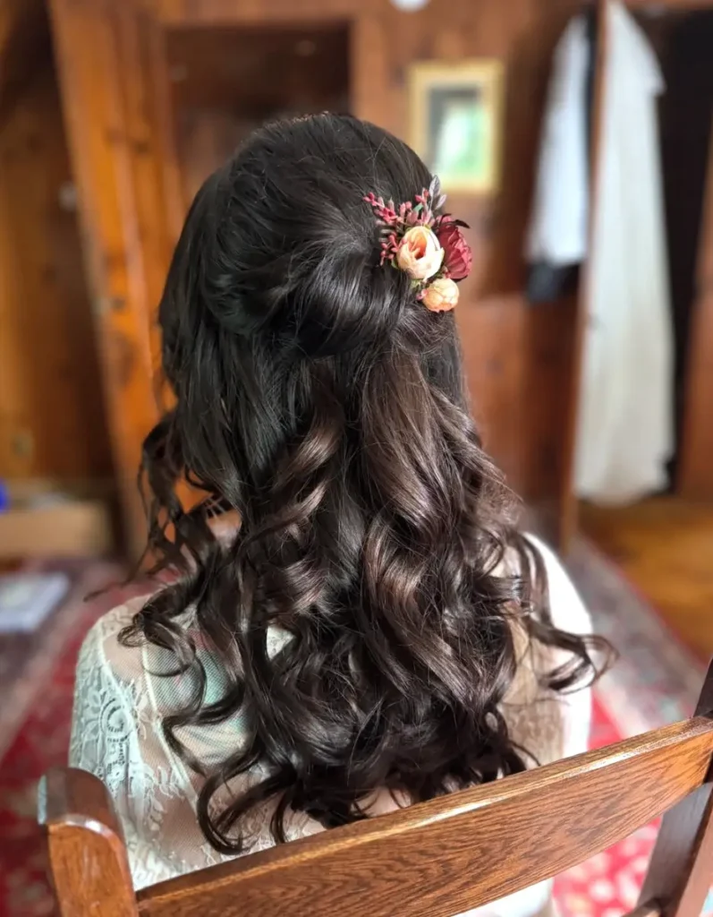 - Marion Salon Spa in Salt Point, NY Close-up of the back of a woman's dark hair styled in a half-up look with soft cascading curls and a floral hairpiece, a bridal style enhanced with hand-tied hair extensions. - Marion Salon Spa in Salt Point, NY