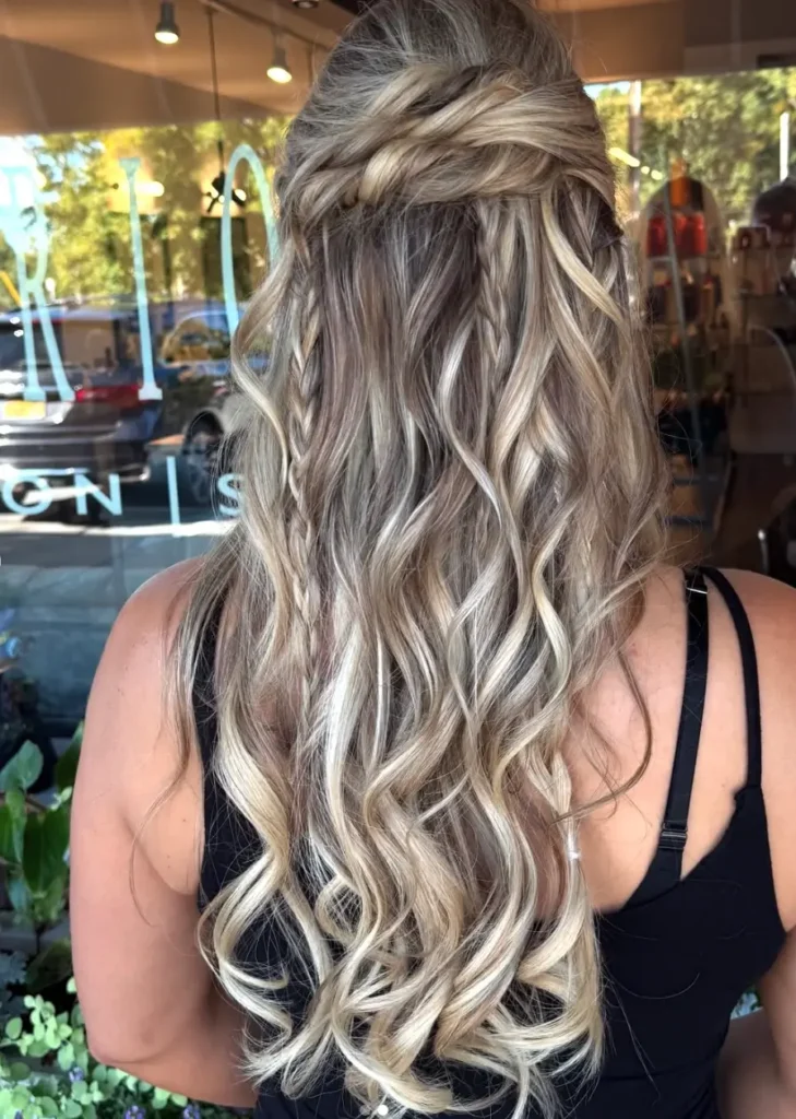- Marion Salon Spa in Salt Point, NY Close-up of the back of a woman's long, wavy hair cascading down in soft curls with dimensional blonde highlights, showcasing the added length and volume of hand-tied hair extensions paired with the balayage hair color technique. - Marion Salon Spa in Salt Point, NY